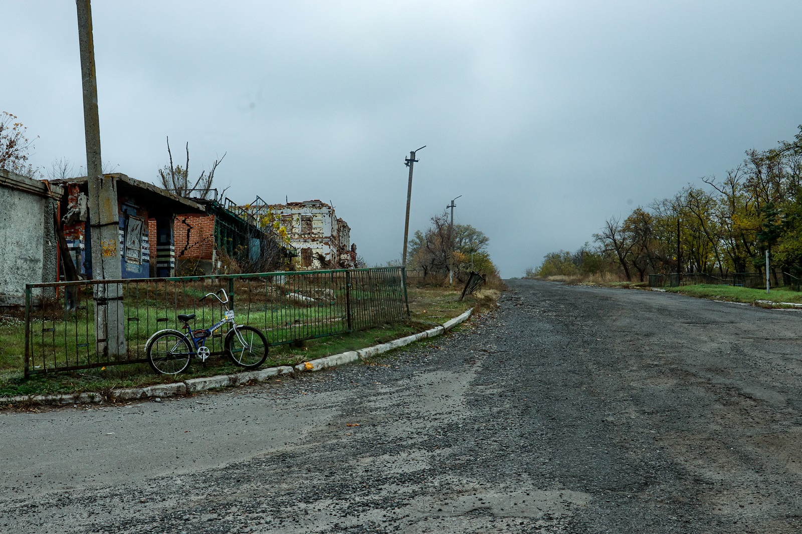 A bike attached to a fence in a street of Ukraine. Behind the fence, houses damaged by explosive weapons