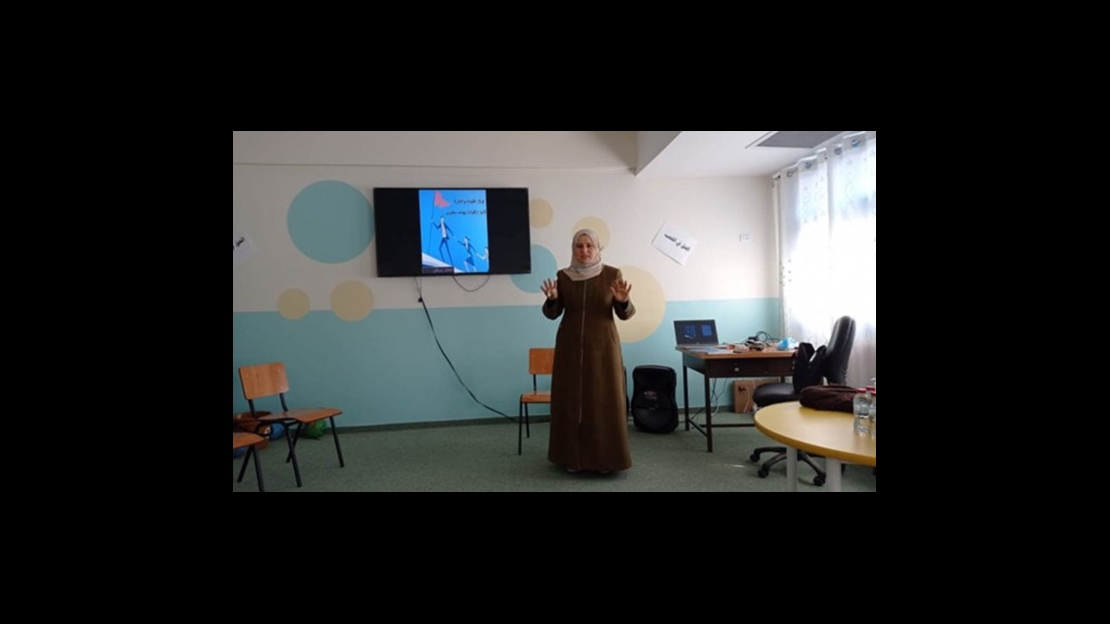 In the West Bank town of Jenin, the headmistress of a boys' elementary school stands in a classroom. Behind her is a television screen.; }}